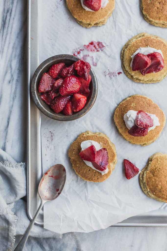 Overhead image of small pancakes with a bowl of strawberries and cream 