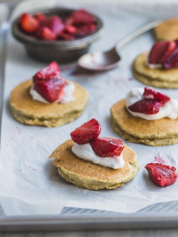 Small coconut banana pancakes with cream and strawberries on a white background