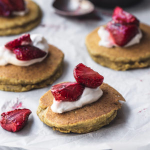 A close up of coconut banana pancakes with cream and strawberries on baking paper