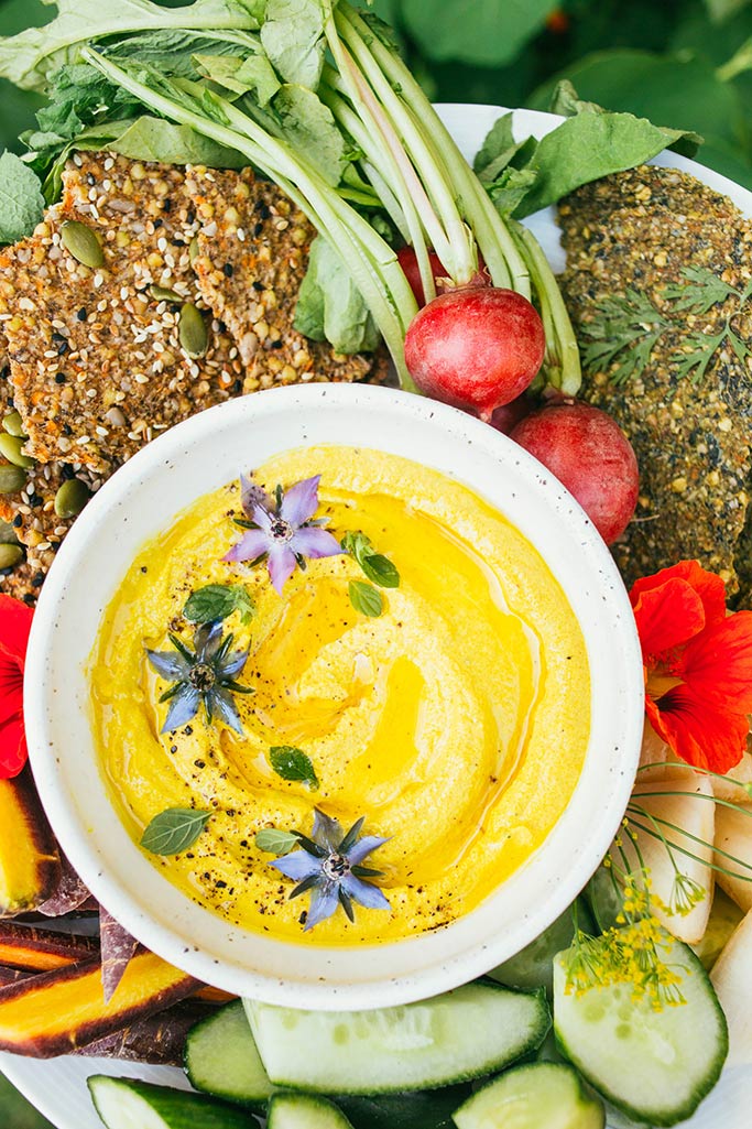 A bowl of yellow dip with fresh vegetables. 