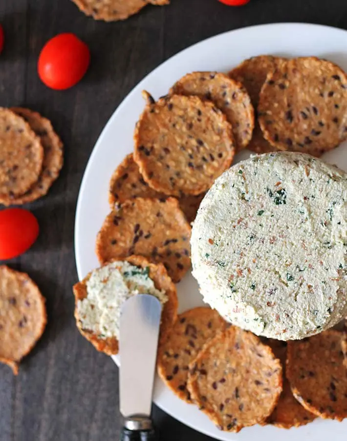 A wheel of cheese with crackers on a plate. 