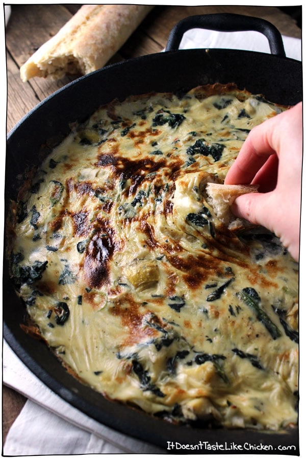 A person dipping bread in to a cheese  and spinach dip. 