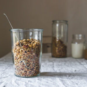 Jar of almond butter maple granola sitting on a white-clothed table, squared image