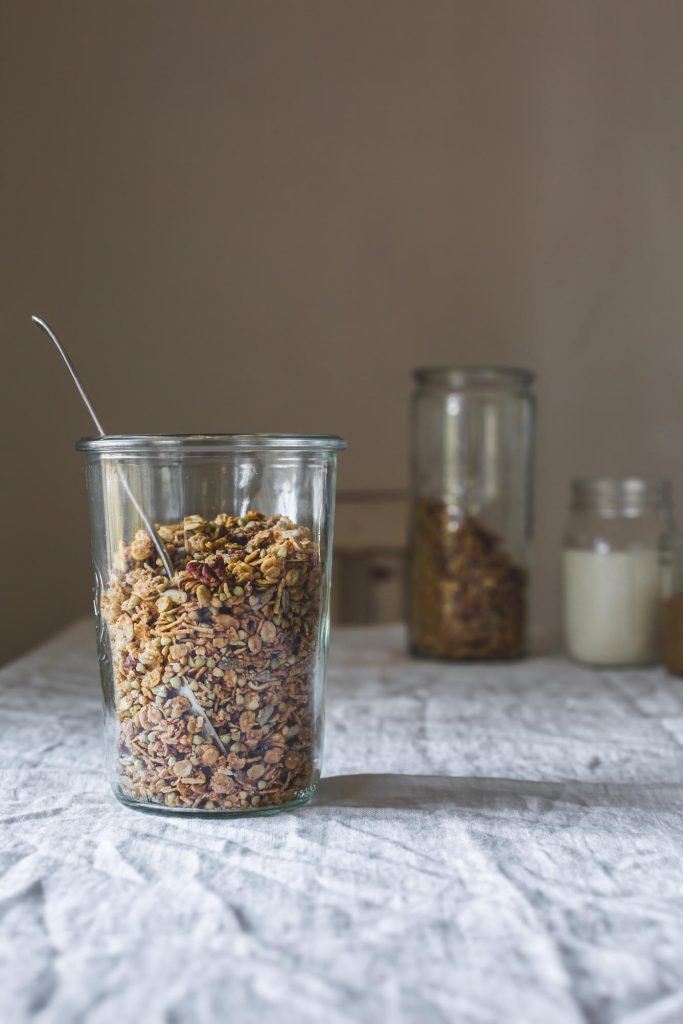 Almond Butter Maple Granola in a glass storage jar sitting on a clothed table
