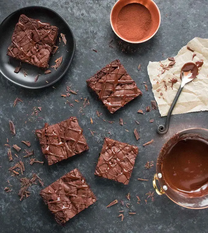 Brownies and melted chocolate on a grey background. 