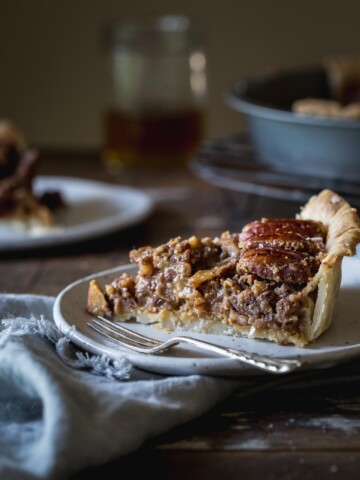 A slice of vegan pecan pie on a plate with a napkin sitting on a wooden table