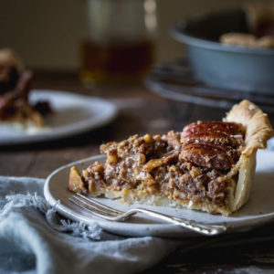 A slice of vegan pecan pie on a plate sitting on a wooden table setting