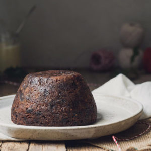 A Christmas pudding on a cream plate sitting on a wooden table