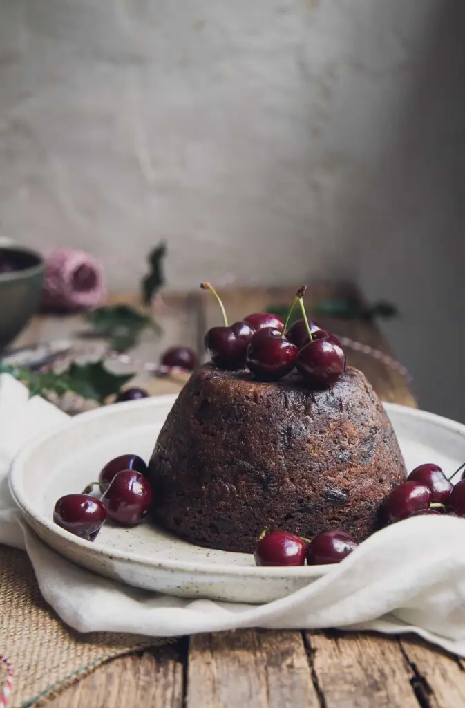 Vegan Christmas pudding on a serving plate with fresh cherries