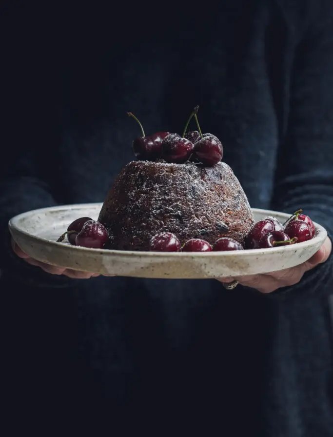 Woman holding a plate with a vegan Christmas pudding and cherries