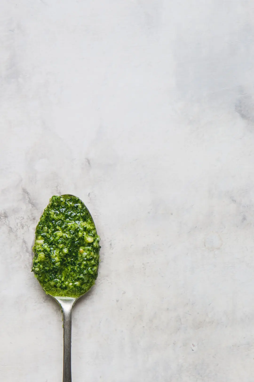 flat lay image of a rustic spoon filled with vegan kale pesto offset to the bottom corner of the image