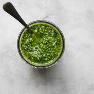 An overhead image of a jar of green kale pesto with a spoon