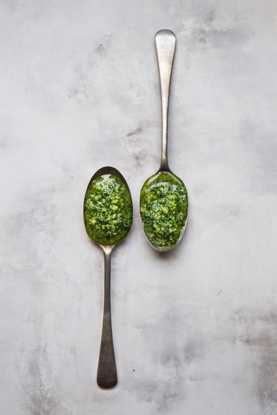 flat lay image of two rustic spoons filled with vegan kale pesto on a marbled tabletop
