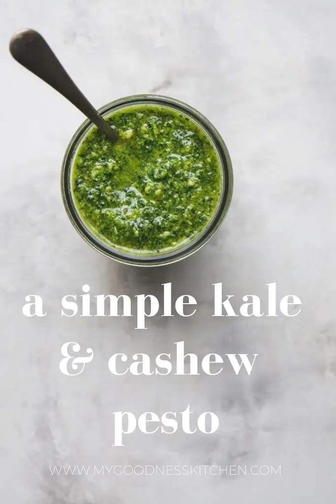 an overhead image of a jar of kale and cashew pesto with a spoon sitting on a marbled light surface. Title text overlay.