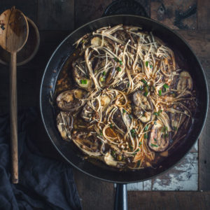 overhead image of a large skillet filled with spicy eggplant stir-fry on a rustic wooden table