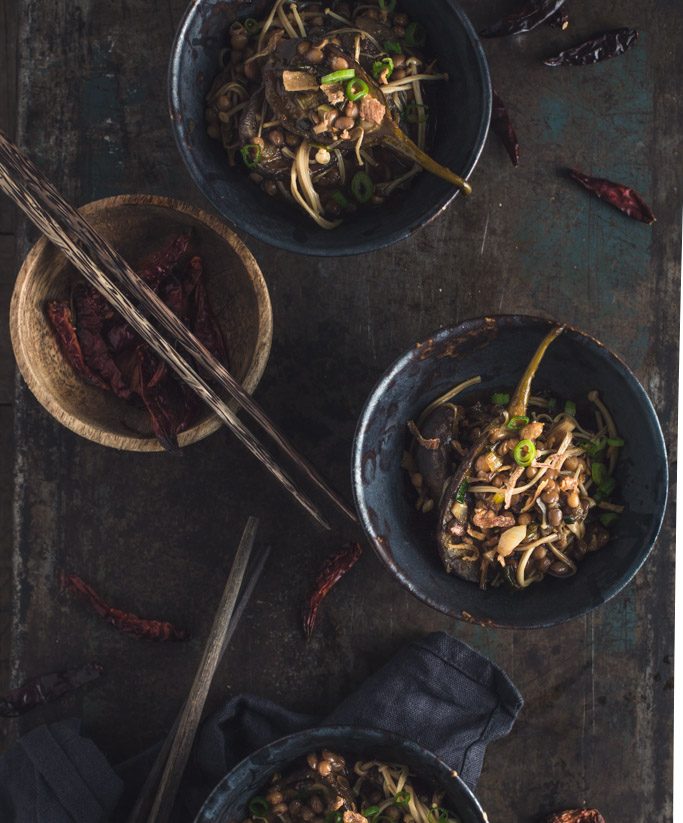 An overhead image of several small bowls of eggplant stir-fry on a rustic metal tabletop