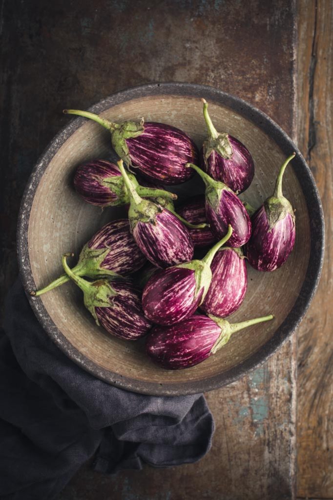 An overhead image of a bowl of the striped small eggplants used in the recipe