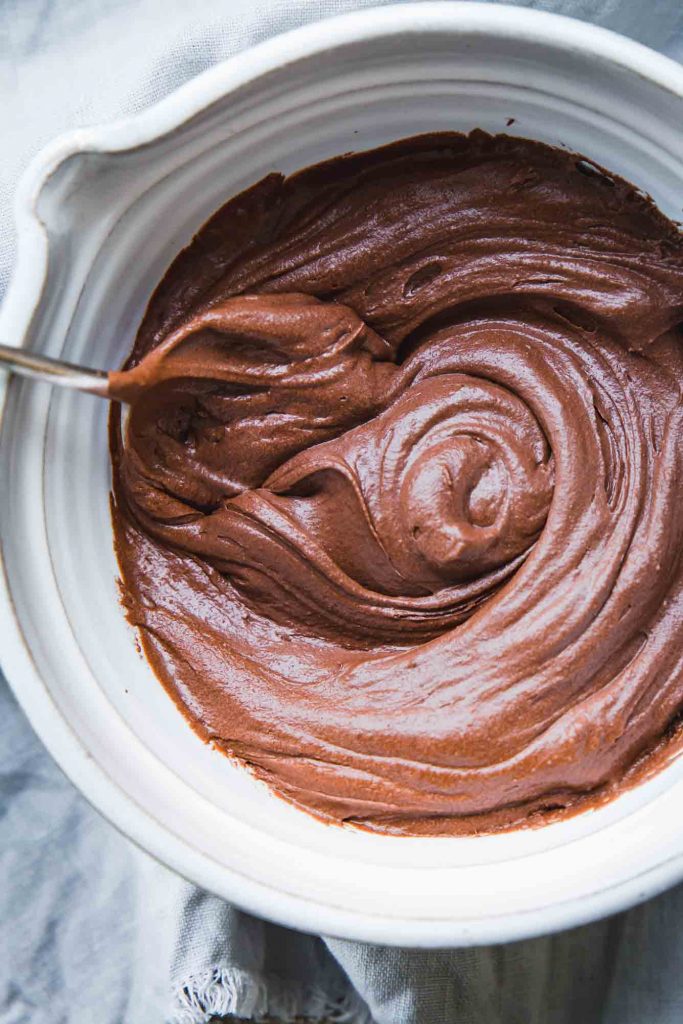 Close-up image of a white mixing bowl full of vegan chocolate frosting swirls