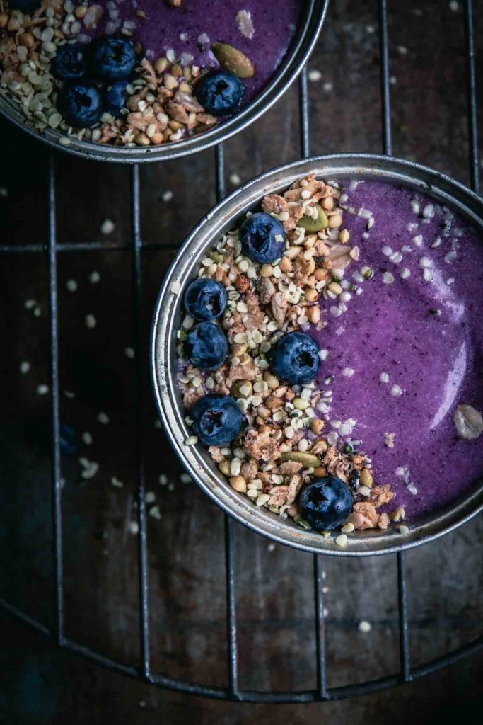 A super close-up image of a blueberry pie smoothie bowl served in a pie tin with granola and fresh berries.