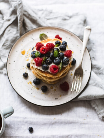 An overhead image of a stack of pancakes on a plate with berries