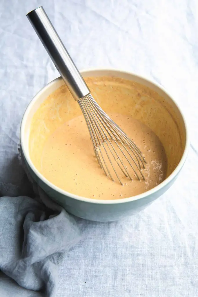 A overhead shot image of an aqua mixing bowl full of vegan pumpkin waffle batter with a whisk sitting inside the bowl