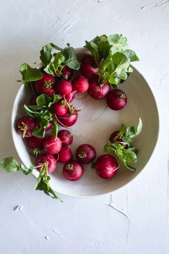 A wreath of freshly washes radishes with their leaves still attached in a rustic white bowl