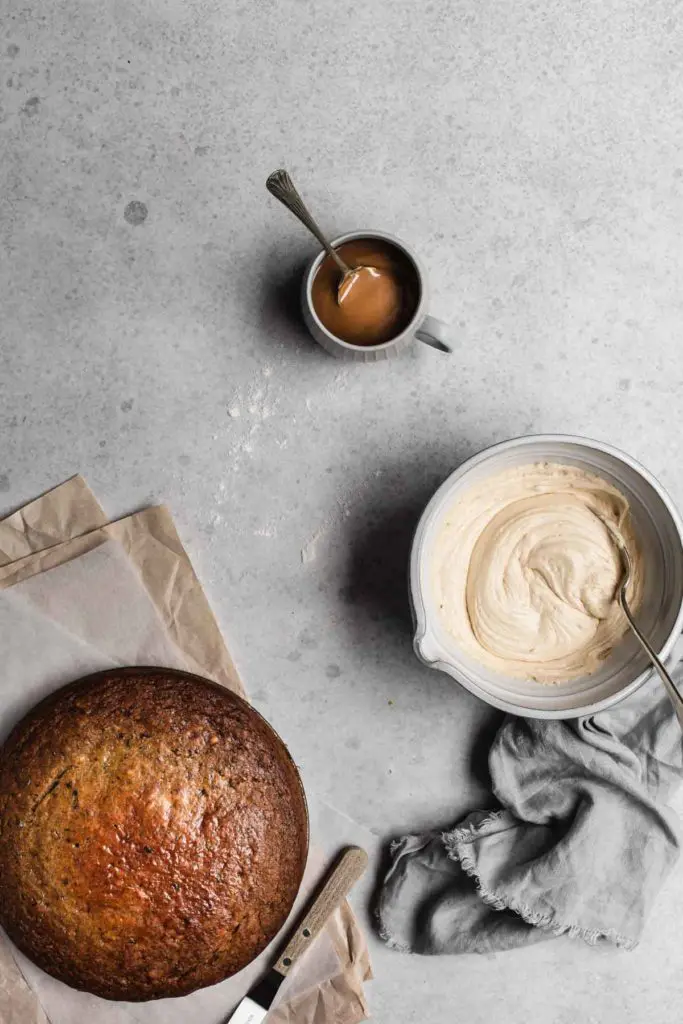 An overhead image of the freshly baked cake, the salted caramel frosting in a bowl and a cup of salted caramel. The cake is ready to decorate.