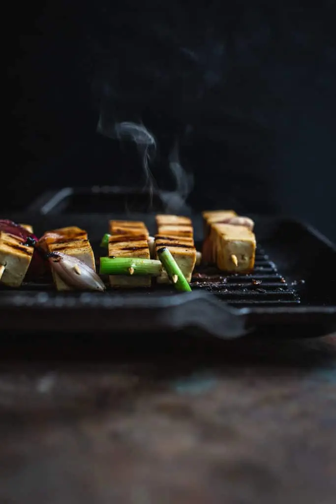 front on image of tofu yakitori grilling on a Lodge grill pan with smoke coming off the pan