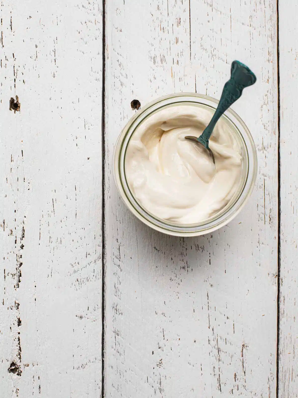 A glass jar full of vegan mayonnaise on a white table.