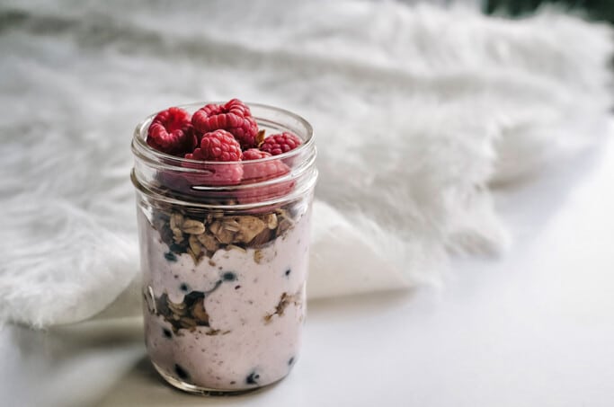 A jar of yoghurt, granola and fruit on a white table