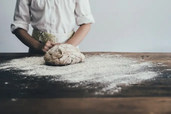 A woman standing behind a table with dough and flour in front