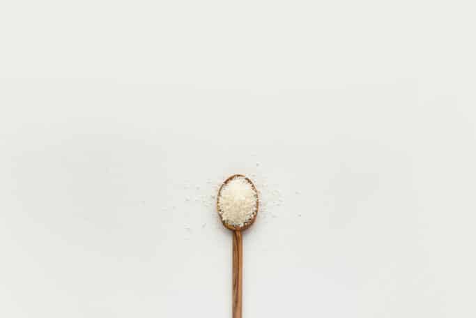 A wooden spoon full of course salt on a white background