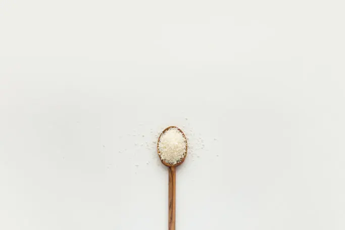 A wooden spoon full of course salt on a white background