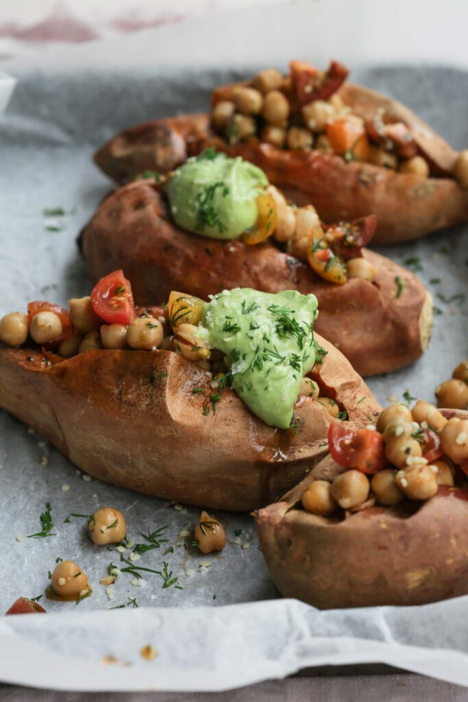 Close up image of finished herbed chickpea stuffed sweet potatoes on a tray with a dollop of green avocado tahini sauce on each