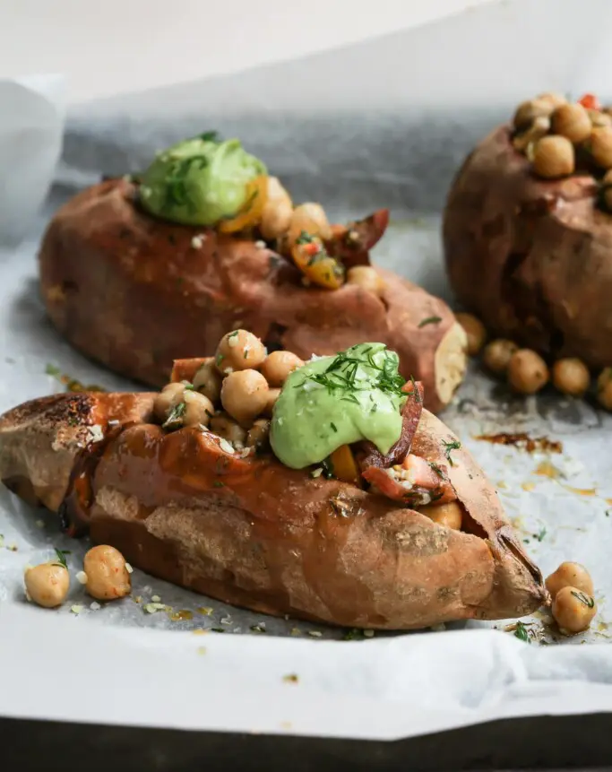 Three herbed chickpea stuffed sweet potatoes on a lined baking tray with the front potato in focus