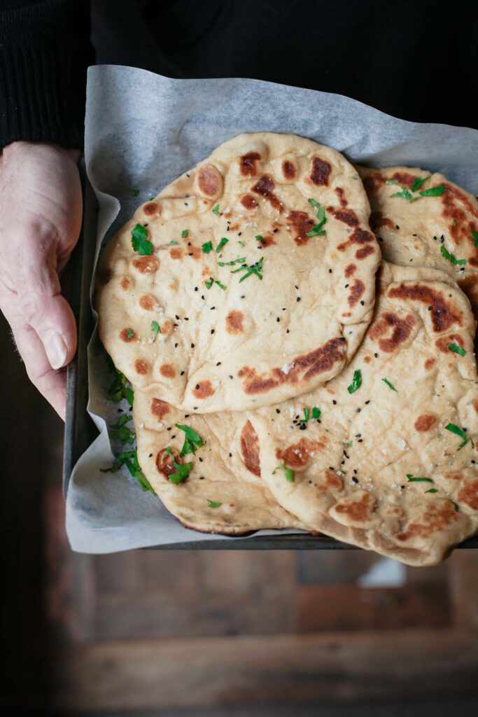 A close up of a person holding a tray of naan breads