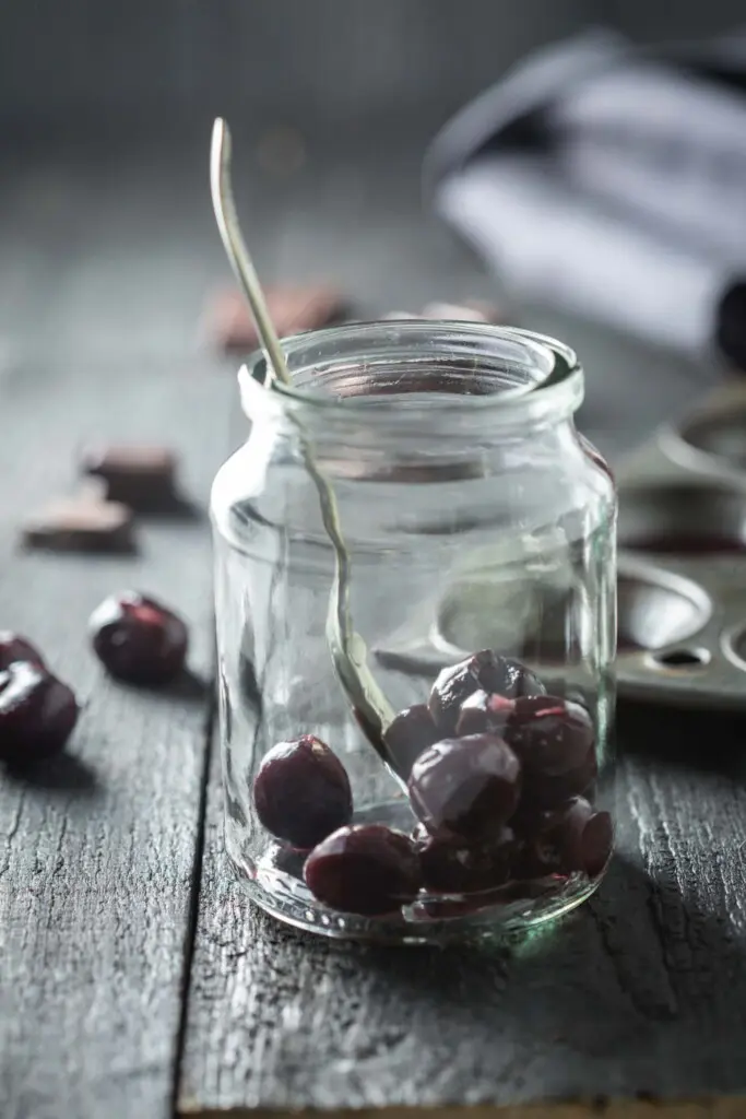 A drinking jar with soaked cherries being placed in the bottom