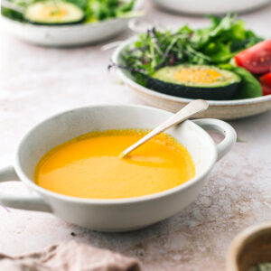 A cropped front on image of a bowl of carrot and ginger dressing with bowls of salad in the background