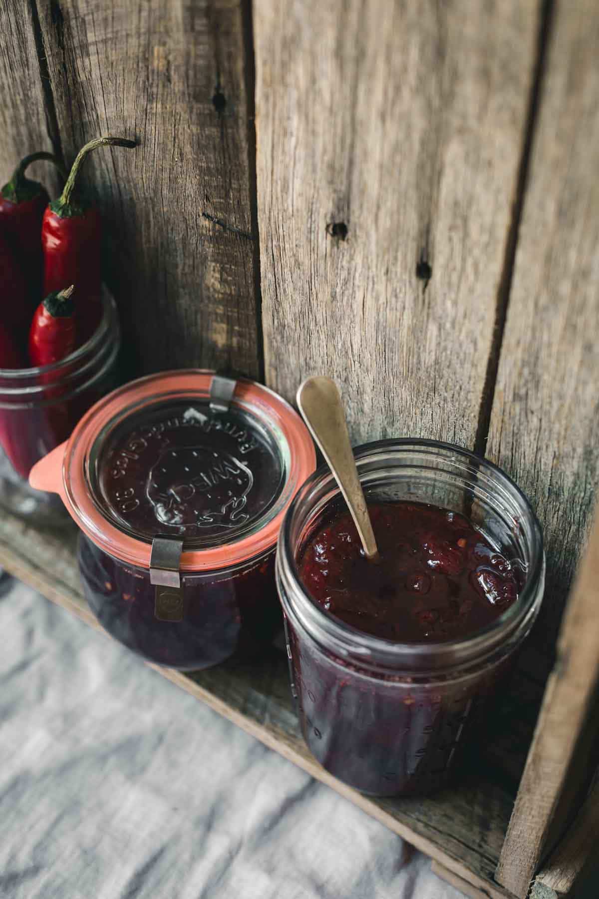 An open jar of jam and other jam jars sitting on a wooden shelf. 