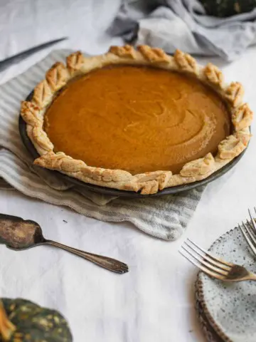 A set table with a pumpkin pie in the middle.