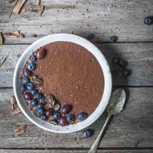 A bowl of chocolate chia pudding with fruit on a wooden table.