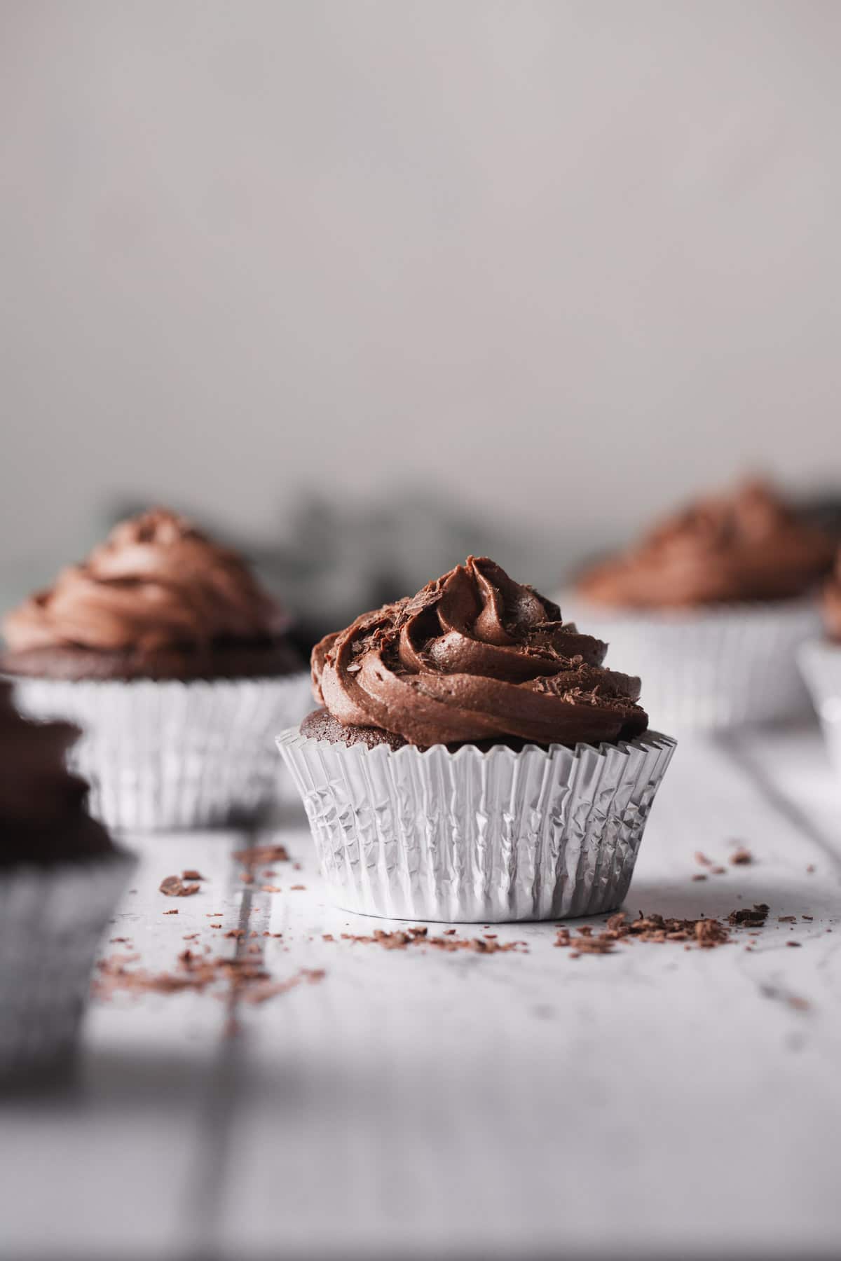 Schokoladen-Cupcakes in silbernen Halterungen auf einem weißen Holztisch.