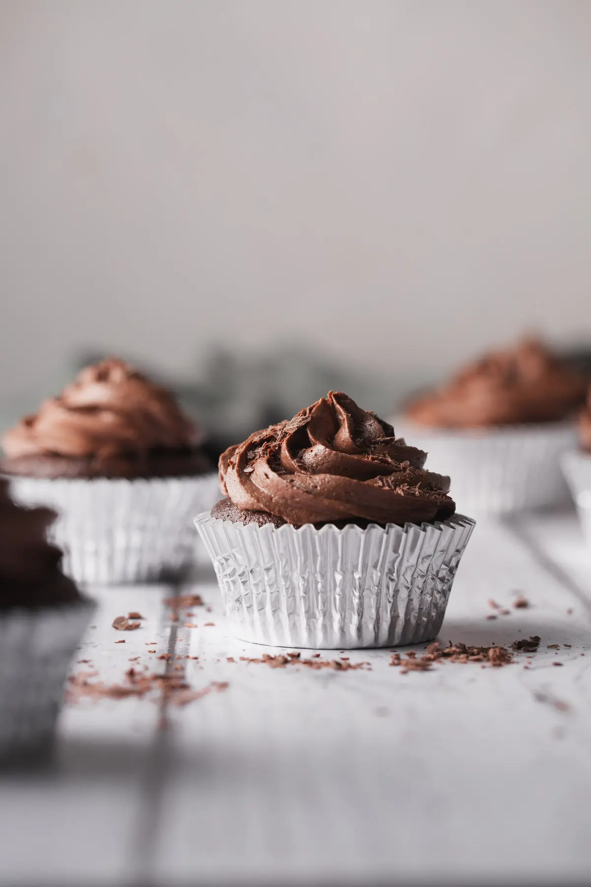 Chocolate cupcakes in silver holders sitting on a white wooden table.