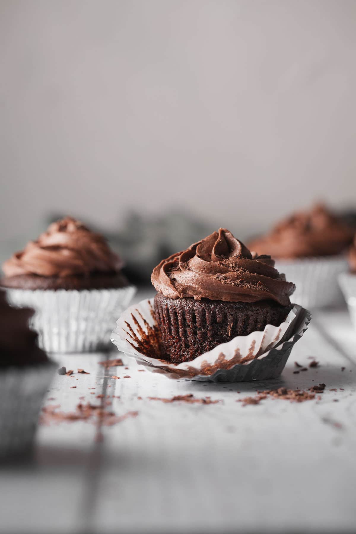 A chocolate cupcakes with the paper holder pealed back to show the cake.