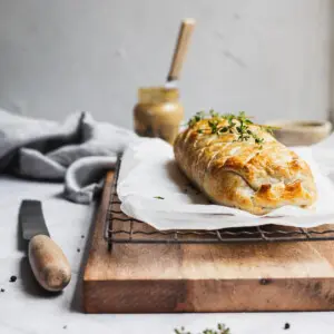 Baked Wellington sitting on a wooden board with mustard.