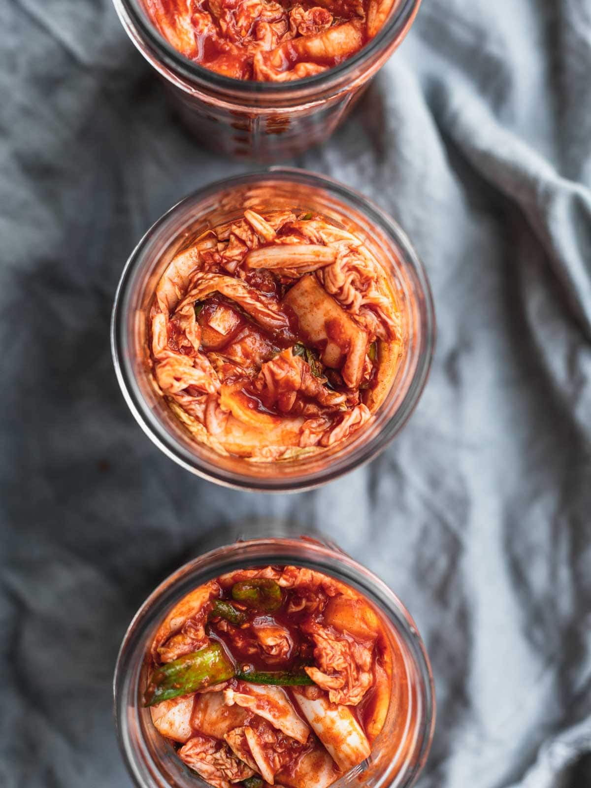 Homemade kimchi in jars on a blue textured cloth.