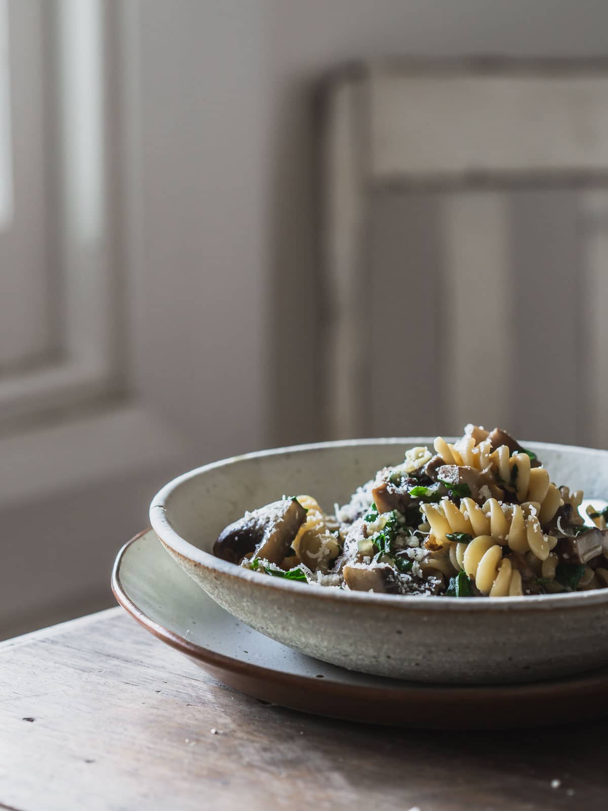 A bowl of mushroom pasta on a wooden table near a window.