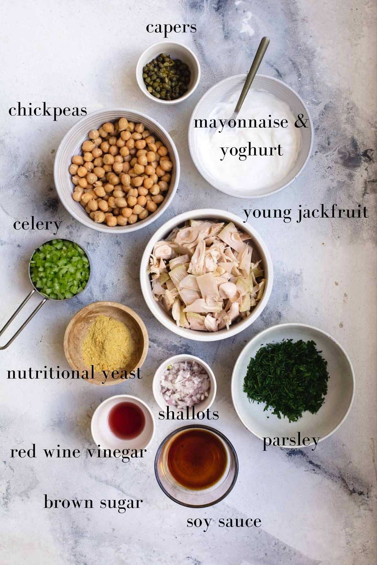 Ingredients for a vegan chicken salad in bowls on a marble background with labels.