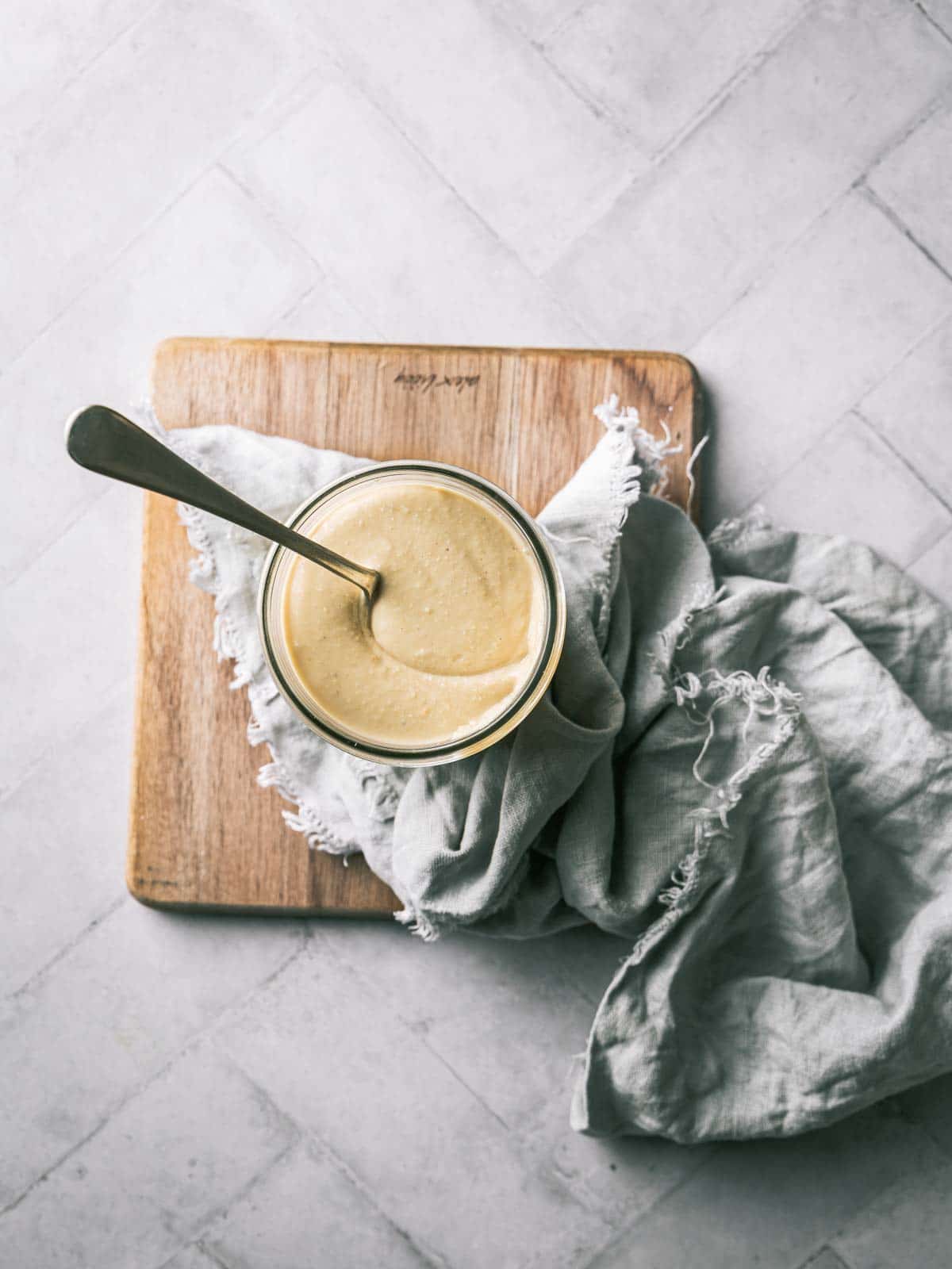 A jar of nut butter on a wooden board with a spoon.