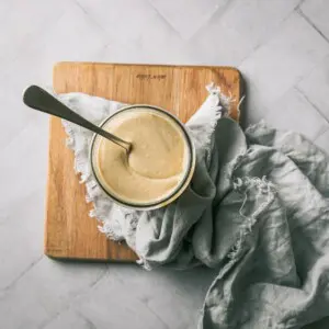 A jar of cashew butter on a wooden board with a spoon.